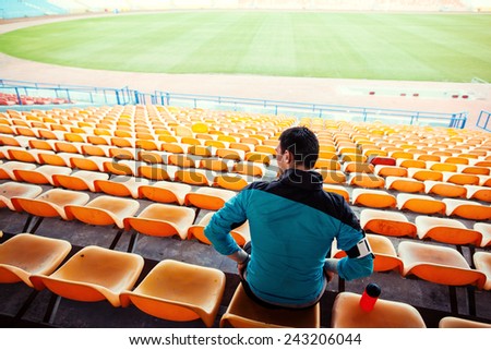 sportsman with a bottle of water sitting on the chairs in the track and field stadium