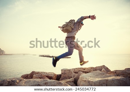brave man with backpack running over rocks near ocean in sunset