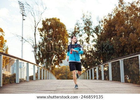 young sportsman wearing shorts running in the park over wooden bridge