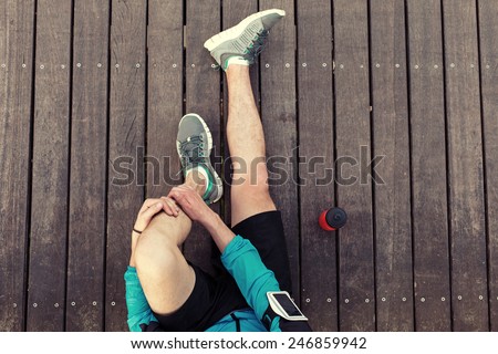 resting sportsman\'s legs sitting on the wooden floor with red sport plastic bottle, view from the top