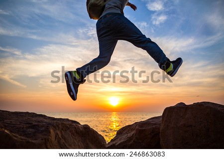 traveler jumping over rocks near the ocean at beautiful sunset