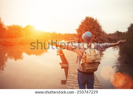 happy traveler on the lake with outspread hands looking at sunset