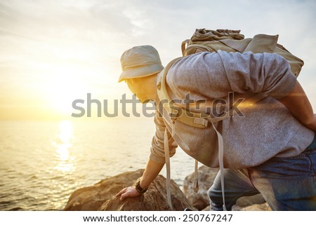 traveling man with backpack near the ocean looking far away at sunset