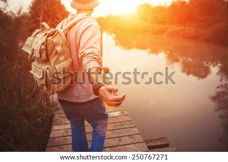 traveler with backpack walking over wooden bridge on the lake in sunset