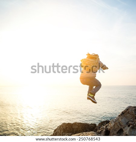 brave man with backpack jumping over rocks in sunset