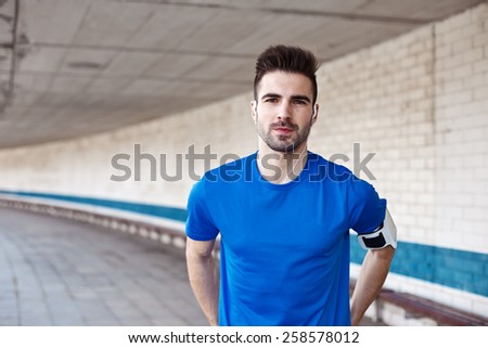 Portrait of handsome male athlete with stubble in blank t-shirt and earphones