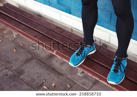 close-up of athlete's legs with blue running shoes standing on bench