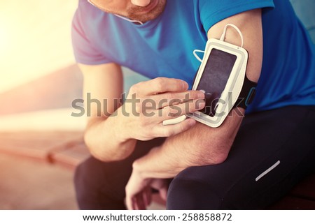 athlete listening music and touching armband for smartphone (intentional sun glare)
