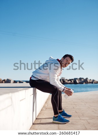 tired athlete sitting and resting near the water after doing workout