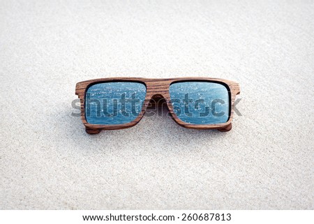 double exposure of wooden sunglasses and blue ocean with white sand background