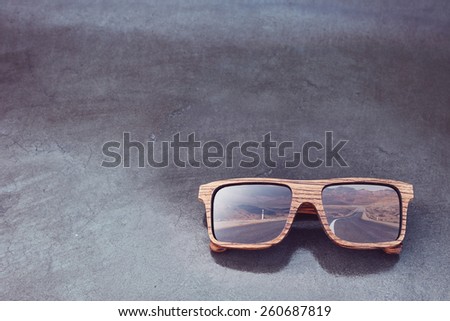 double exposure of wooden sunglasses and desert road with concrete glossy background