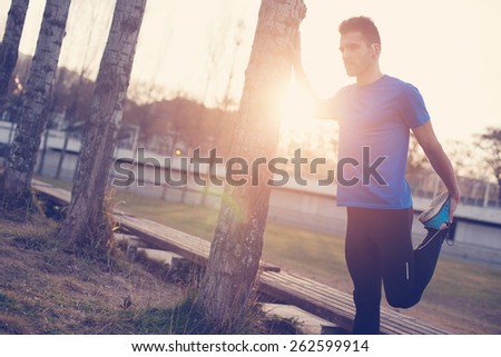 Male athlete doing stretching muscles for running in the park at sunset (intentional sun glare and vintage color)