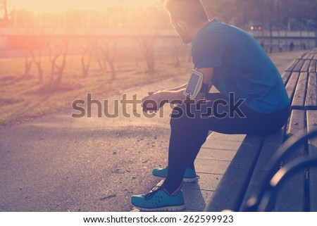 Male athlete restin on bench in park at sunset after running with bottle of water (intentional sun glare and vintage color)