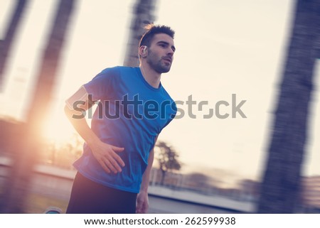 Close-up athlete running in the park along trees at sunset (strong motion blur, intentional sun glare and vintage color)