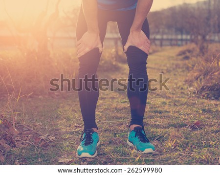 Tired athlete standing in park at sunset and resting (intentional sun glare and vintage color)