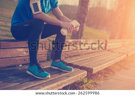 Tired athlete resting on the bench in park with bottle of water (intentional sun glare and vintage color)