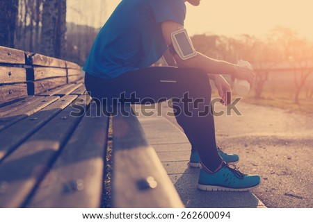Athlete restin on bench in park at sunset after running with bottle of water (intentional sun glare and vintage color)