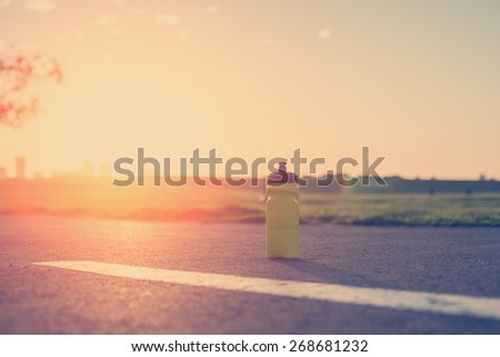 plastic sport flask with water and minerals on the road in park at sunset (intentional sun glare and vintage color)
