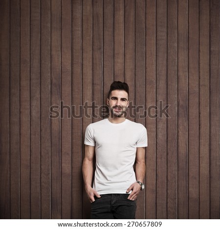 Smiling man in white blank t-shirt, dark wooden wall background
