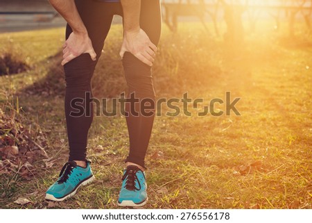 Tired athlete standing in park at sunset and resting (intentional sun glare)