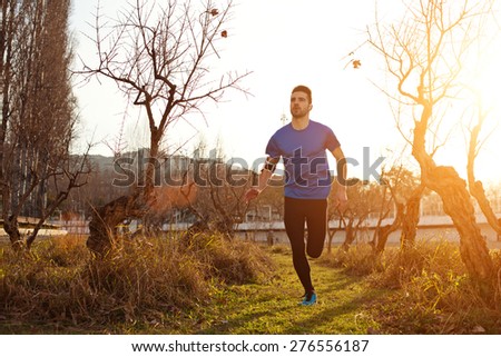 Handsome young athlete jogging in the park at sunset (little motion blur, intentional sun glare)