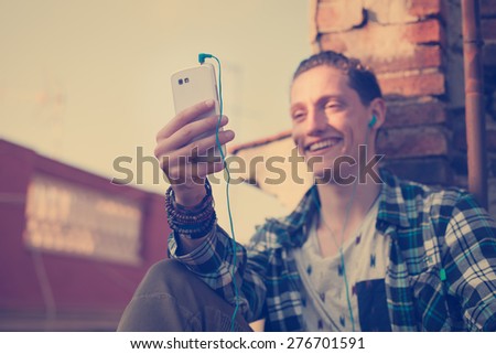 Young and smiling man on the roof, looking at mobile phone and listening music (intentional vintage color, focus on mobile phone)