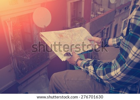 Brave young man sitting on the edge of high roof with map in hands (intentional sun glare and vintage color, focus on map)
