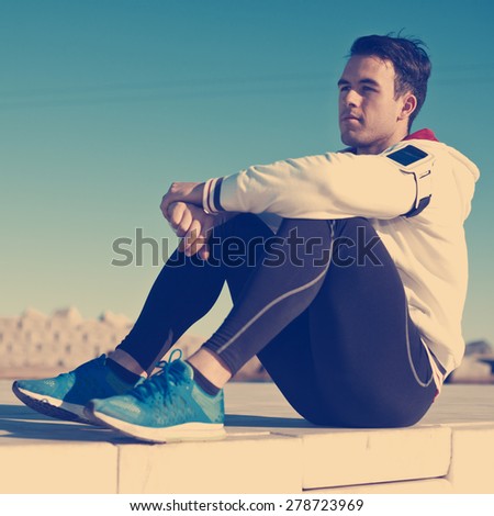young and handsome athletic man with armband relaxing after fitness outdoors (intentional vintage color)