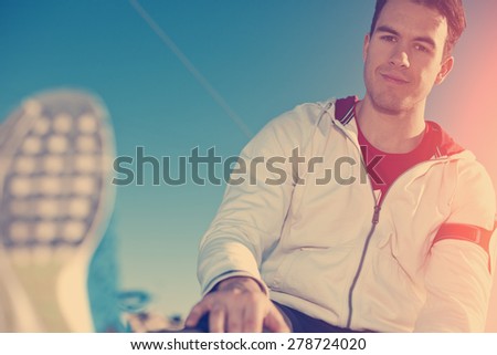 young and handsome athlete with armband relaxing after fitness outdoors (intentional sun glare and vintage color)