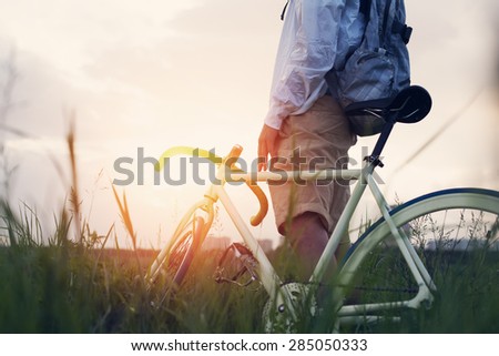 young man with bicycle in the green field at sunset (intentional sun glare and dark colors)
