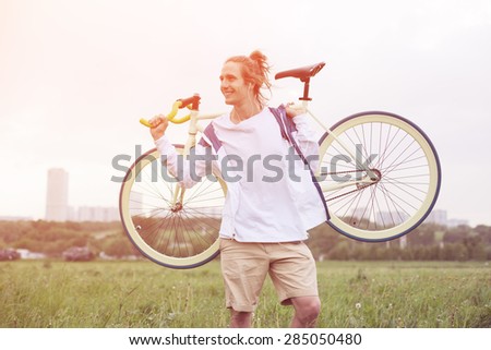 young smiling man in blank t-shirt standing with bicycle (intentional sun glare and bright colors)