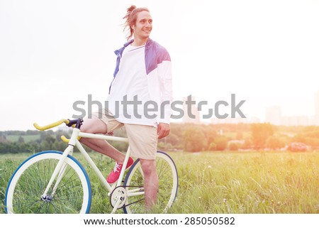 young long hair man in blank t-shirt sitting on his bicycle in the field (intentional sun glare and vintage colors)