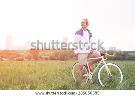 young and handsome man in blank t-shirt sitting on his bicycle in the field (intentional sun glare and vintage colors)