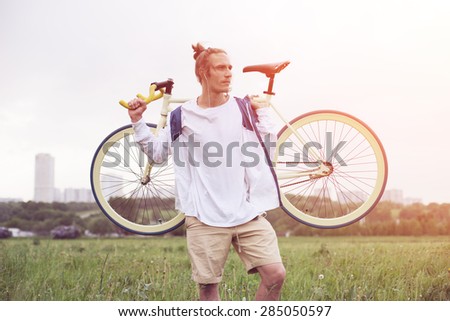 young and handsome man in blank t-shirt standing with bicycle (intentional sun glare and bright colors)