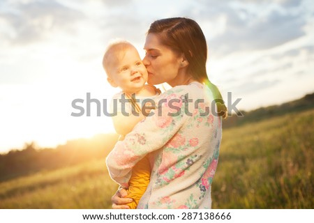 Happy mother kissing her baby in the park (intentional sun glare)