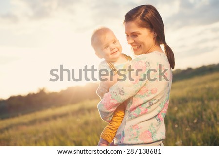 Happy and smiling mother with her baby spending time in the park (intentional sun glare)