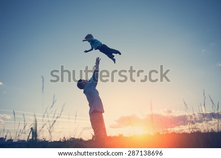 silhouette of father throwing up his son in the park at sunset (intentional sun glare and vintage color)