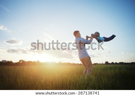 father playing and spinning with his son in the park (intentional sun glare)