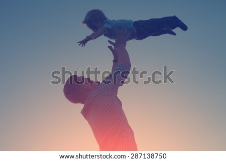 silhouette of father catching and playing with his son in the park in the evening (intentional sun glare and vintage color, lens focus on father)