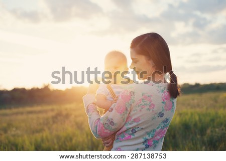 Happy mother with her smiling baby spending time in the park (intentional sun glare)