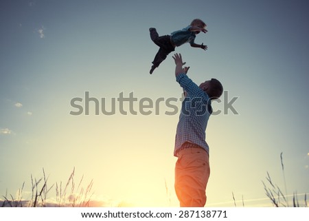 silhouette of father catching his son in the park at sunset (intentional sun glare and vintage color)