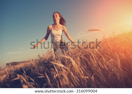 Handsome girl in dress running and having fun in the field at sunset (intentional sun glare)