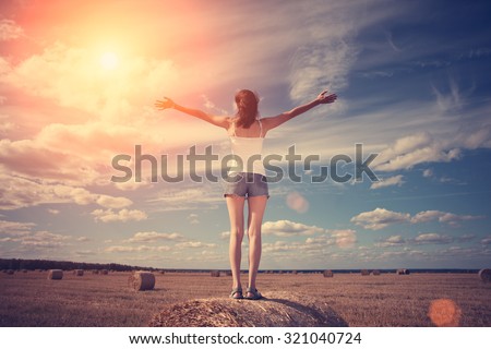 Young girl with outspread hands standing on haystack (intentional sun glare and lens flares)