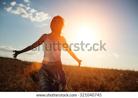 Happy young girl running in the field at sunset (intentional sun glare and lens flares)