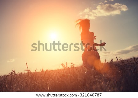 Blurred girl running in the field at sunset (intentional sun glare and lens flares, lens focus on wheat, girl in blur)