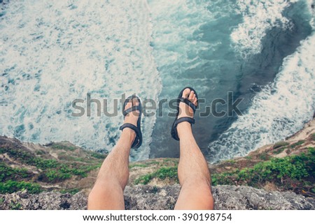 Young brave man sitting on a high cliff above stormy ocean (intentional vintage color, POV view)
