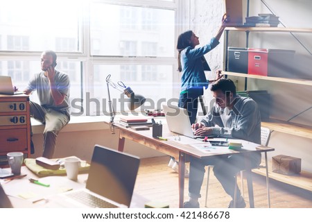 Young startup group working in modern office. Open space, laptops and paperwork. Film effect, blurry background, lens flare effect