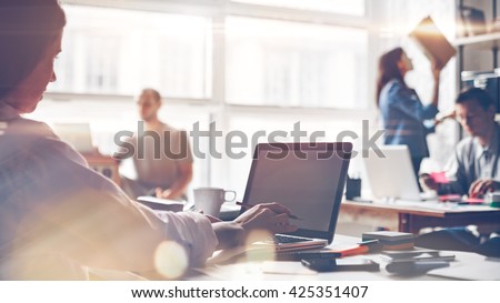 Startup team at work. Big open space office, laptops and paperwork. Business concept. Film effect and lens flare effect, blurry background