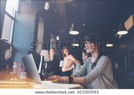Young woman with laptop at workplace. Group of young business people working together. Big open space office. Four persons. Intentional lens flares