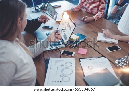 Young business team working together. Group meeting in the office. Paperwork and laptop on the table. Woman pointing to the screen. Four people. Intentional lens flares